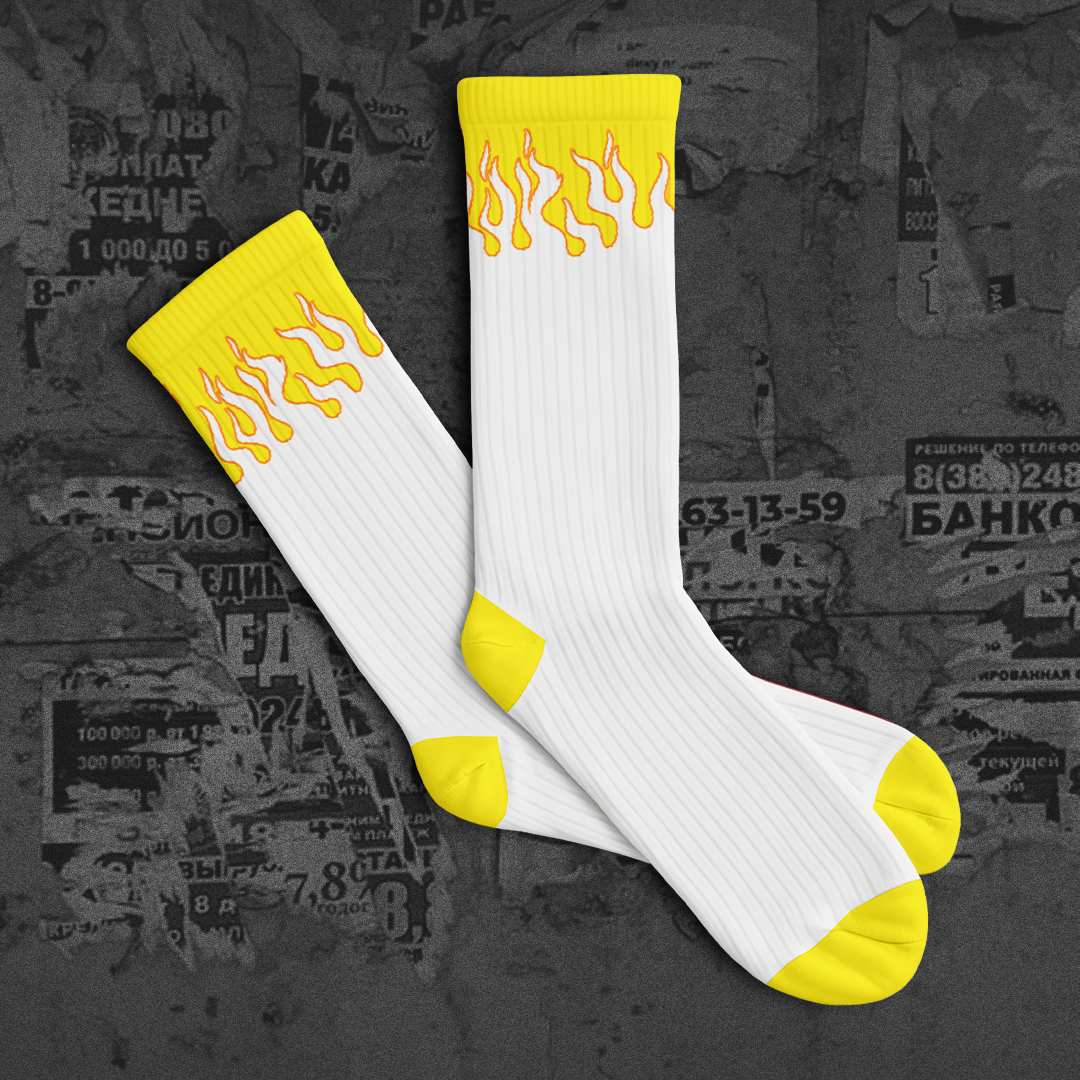 White socks with yellow flame patterns on a dark textured background with 'NEW DROP' text.